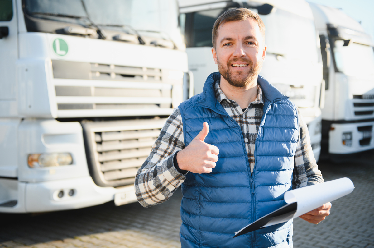 a professional holding a clipboard giving a thumbs up with buses parked behind him